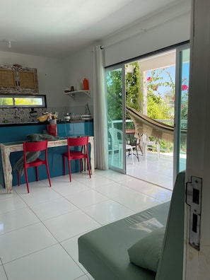 A modern kitchen with blue cabinets, a dining area with red chairs, and a large sliding glass door leading to a balcony with a hammock. - New Listing (Japaratinga)