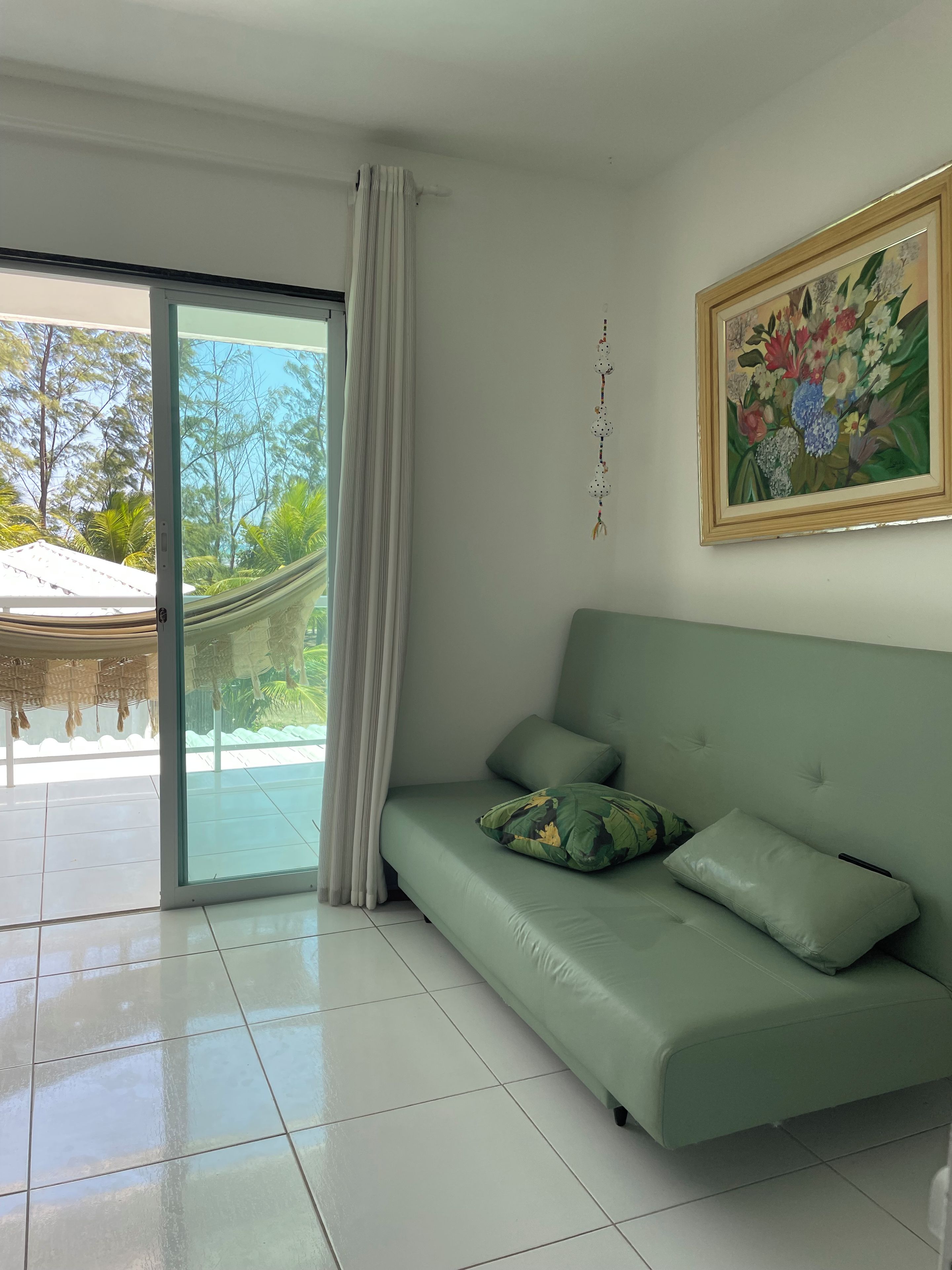 A room with a green sofa, a painting, and a view of a garden through a glass door.