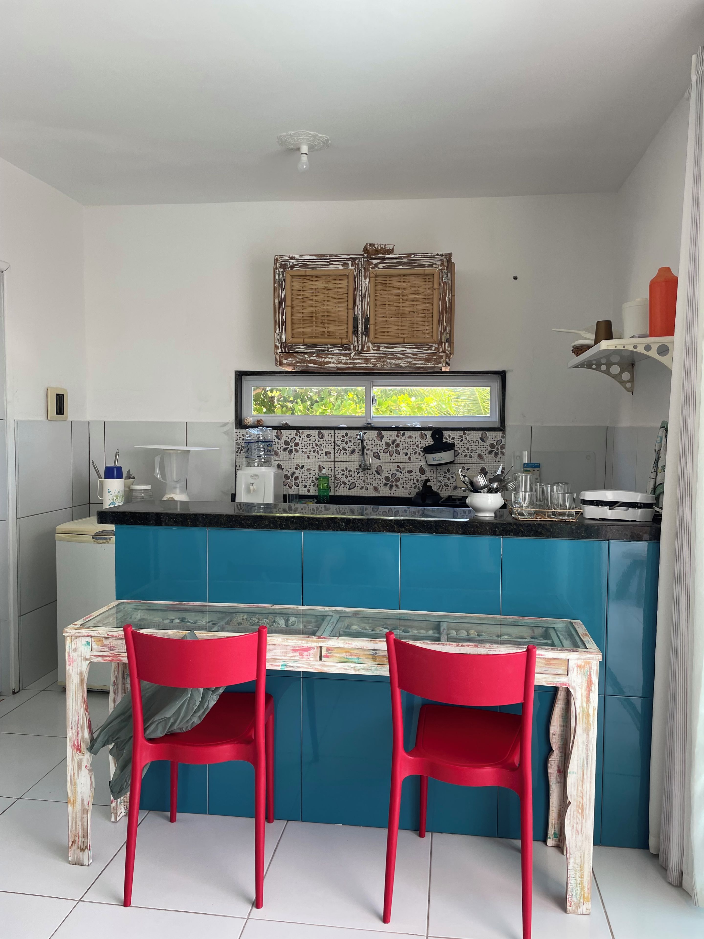 A kitchen with a blue countertop, two red chairs, and a glass table.