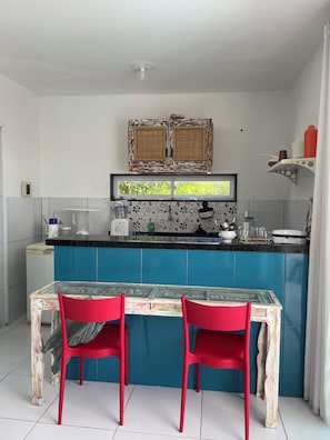 A kitchen with a blue countertop, two red chairs, and a glass table. - New Listing (Japaratinga)