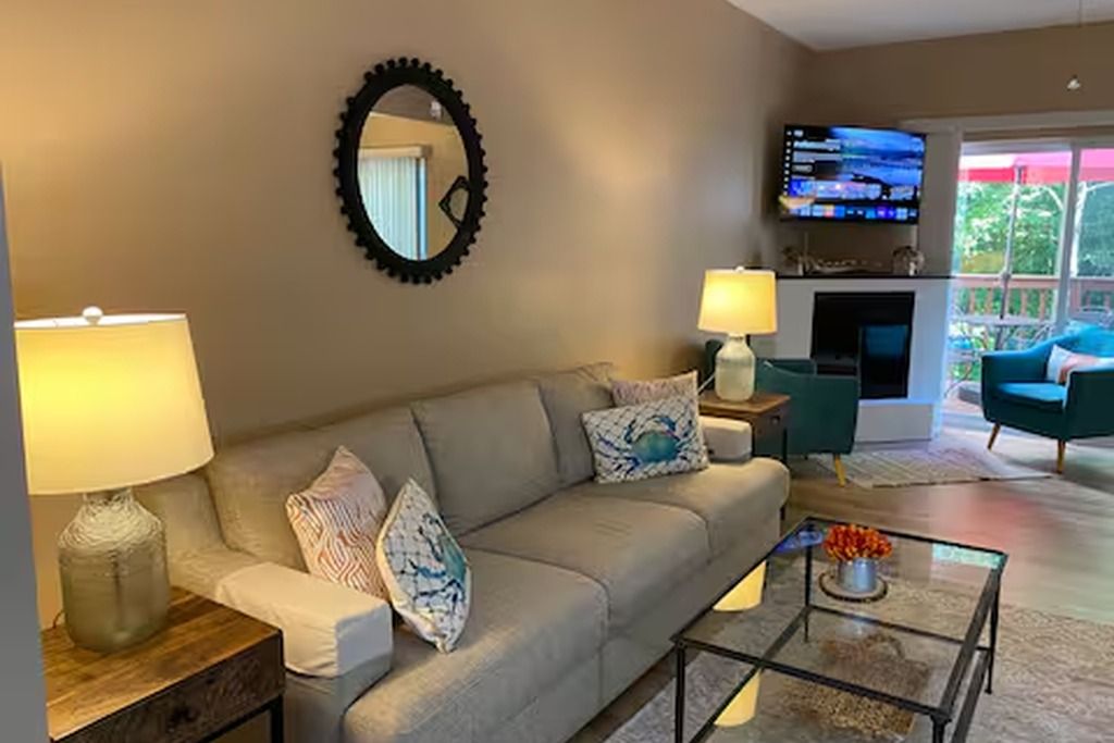 A living room with a sofa, two lamps, a coffee table, and a flat-screen TV mounted on the wall.