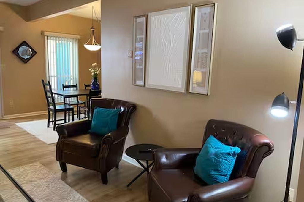 A living room with two leather armchairs, a dining table with chairs, and a floor lamp.