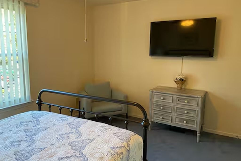 A bedroom with a bed, a television mounted on the wall, a chair, and a dresser.