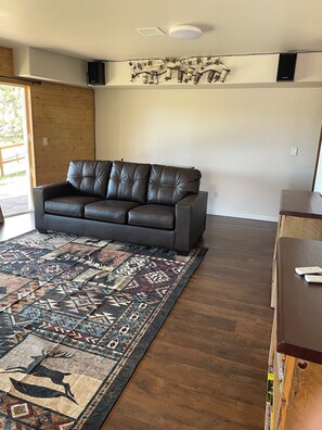 A living room with a dark brown leather sofa, a patterned rug, and a wooden floor. - Quincy's Mountain Cabin Getaway with spectacular views and peaceful serenity! (Florissant)