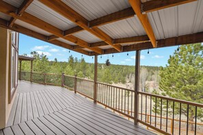 A covered wooden deck with a metal railing, overlooking a forested area. - Quincy's Mountain Cabin Getaway with spectacular views and peaceful serenity! (Florissant)