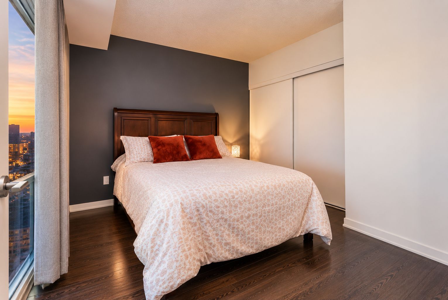 A bedroom with a large bed, a city view, and a window with curtains.