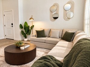 A living room with a sofa, a coffee table, a floor lamp, and a potted plant. - The Napa Luxe Brand-New 2BR/2BA Sleeps 6. (Napa)