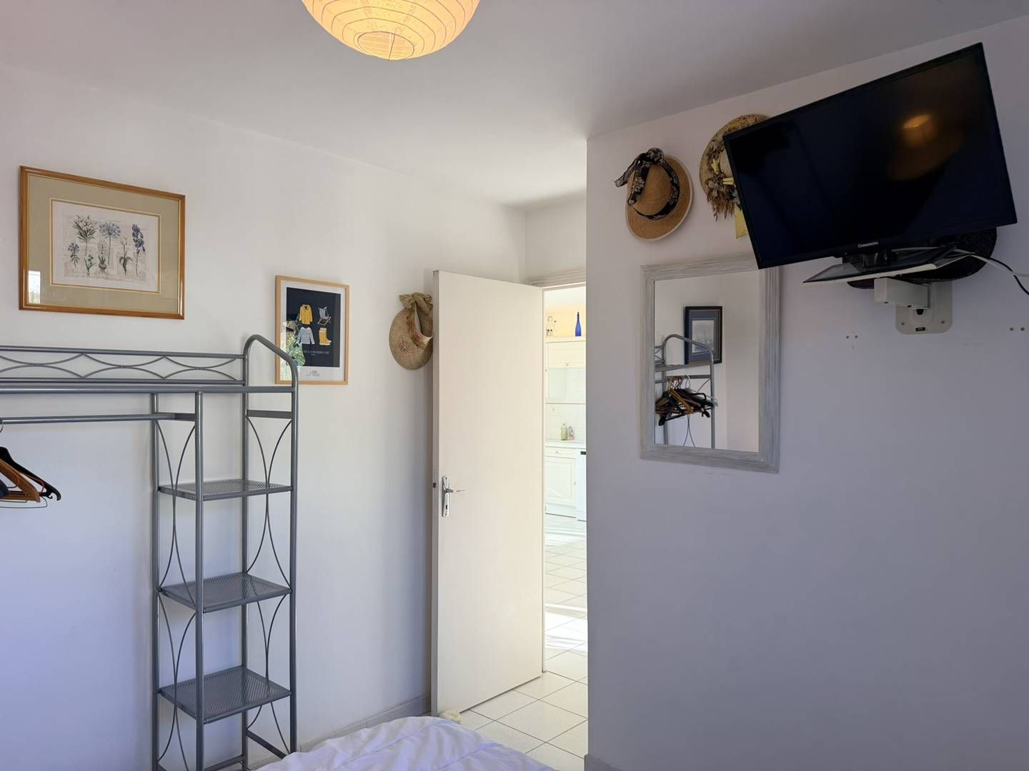 Une chambre avec une étagère en métal, un téléviseur fixé au mur et une porte donnant sur une autre pièce.