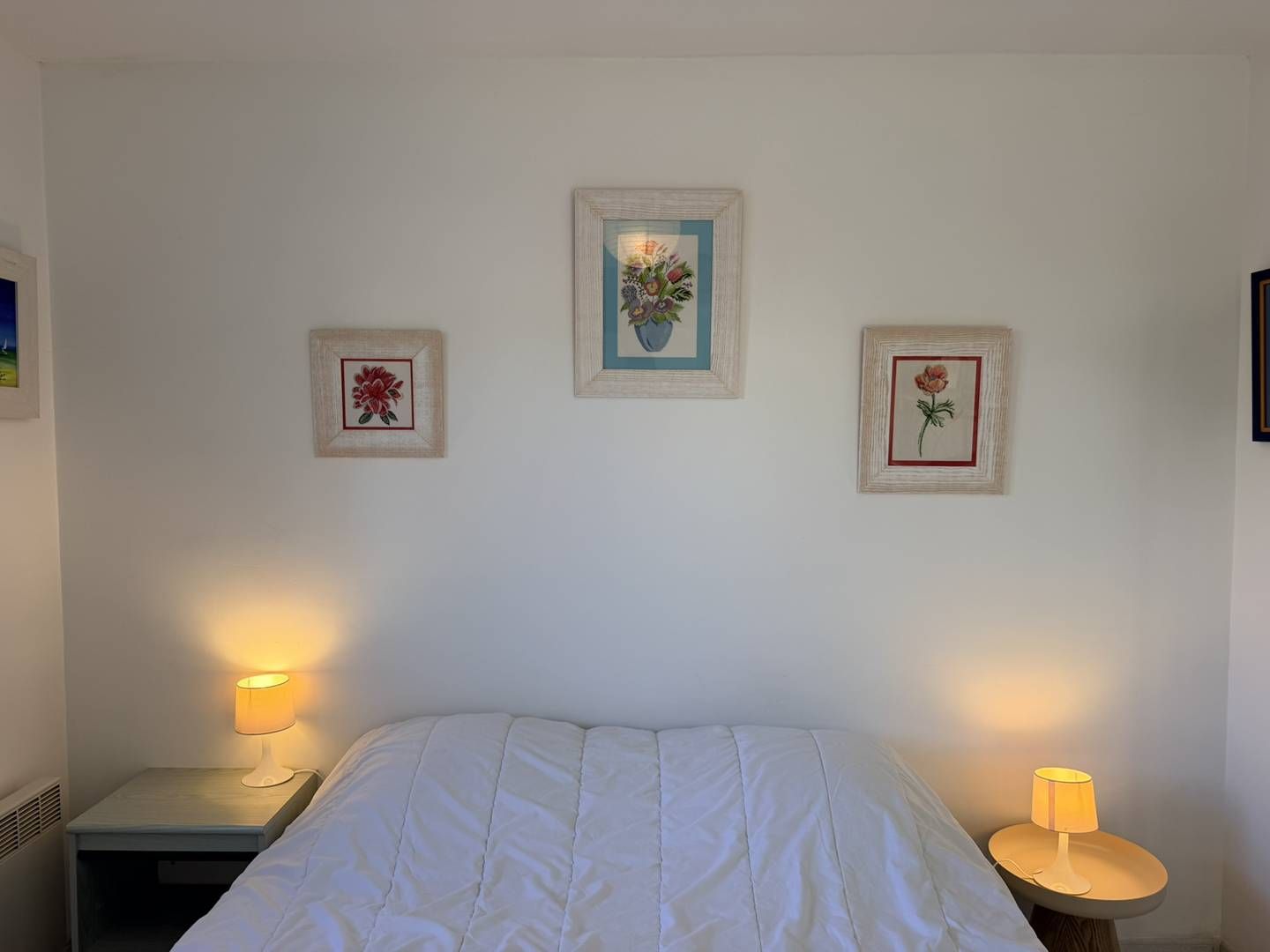 Une chambre à coucher avec un lit, deux tables de chevet et trois tableaux encadrés accrochés au mur.