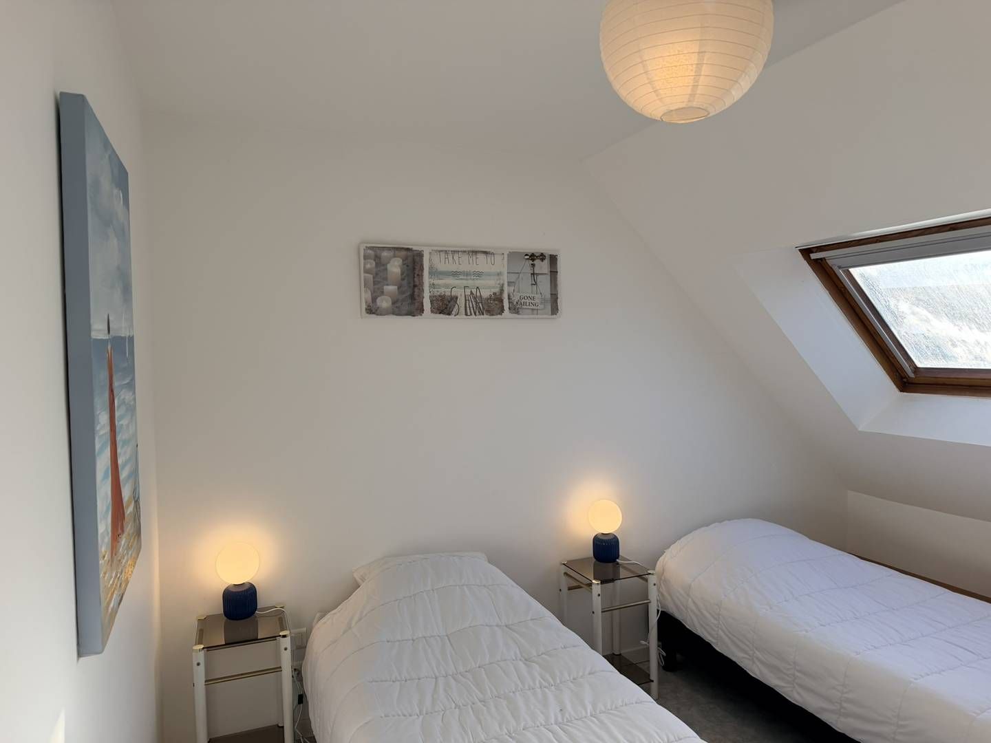 Ein Schlafzimmer mit zwei Betten, einem Oberlicht, einem Wandbild und einer Nachttischlampe.