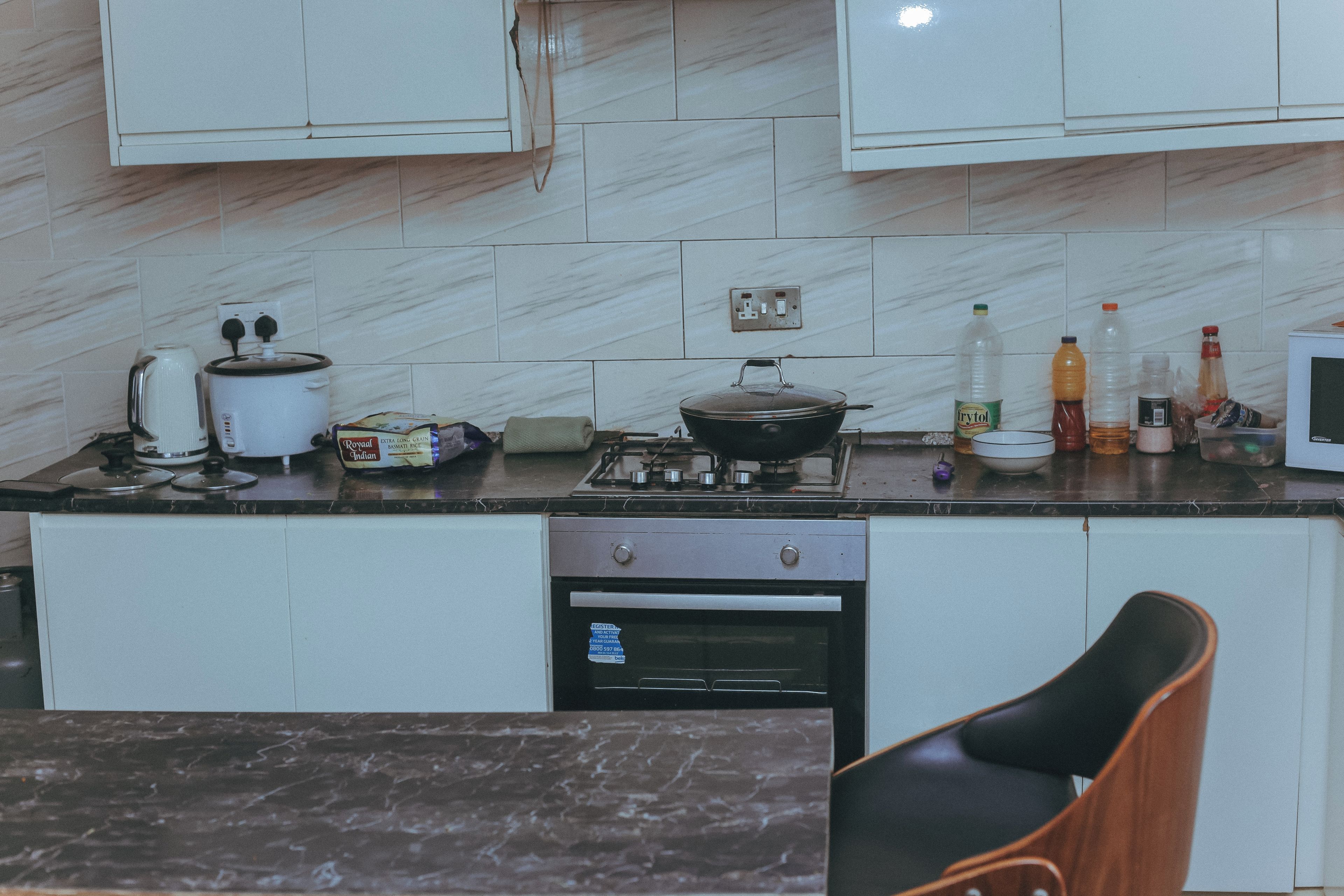 Una cocina con estufa, cocedor de arroz, microondas y varios utensilios de cocina sobre la encimera.