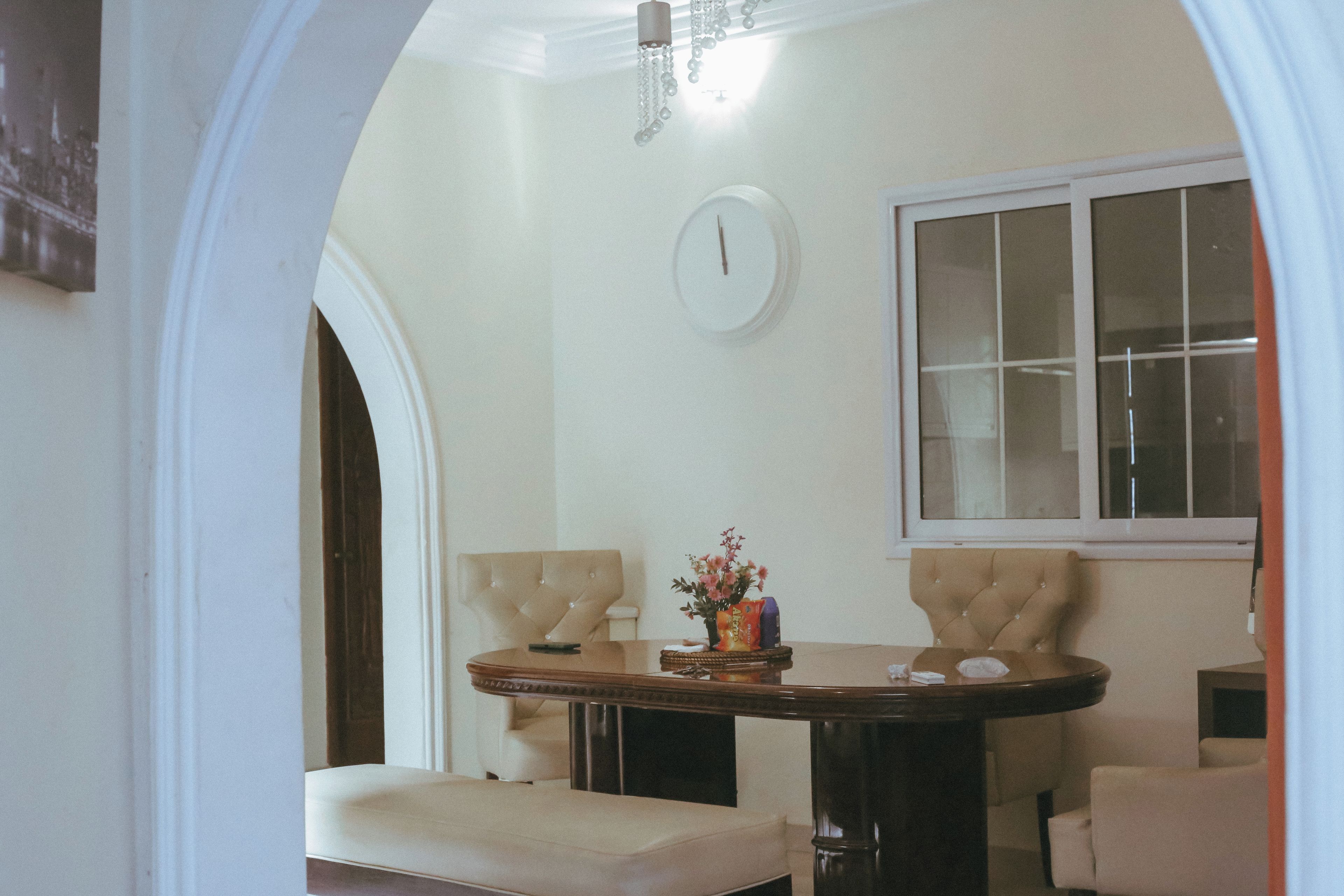 Uma sala de jantar com uma mesa redonda, duas cadeiras, um relógio na parede e uma janela.