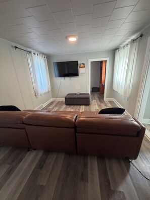 Una sala de estar con un sofá de cuero marrón, un televisor de pantalla plana montado en la pared y piso de madera.