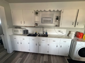 A compact kitchen with white cabinets, a microwave, a toaster, and a washing machine.