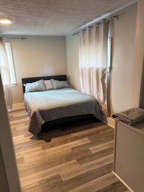 A bedroom with a bed, curtains, and a wooden floor.