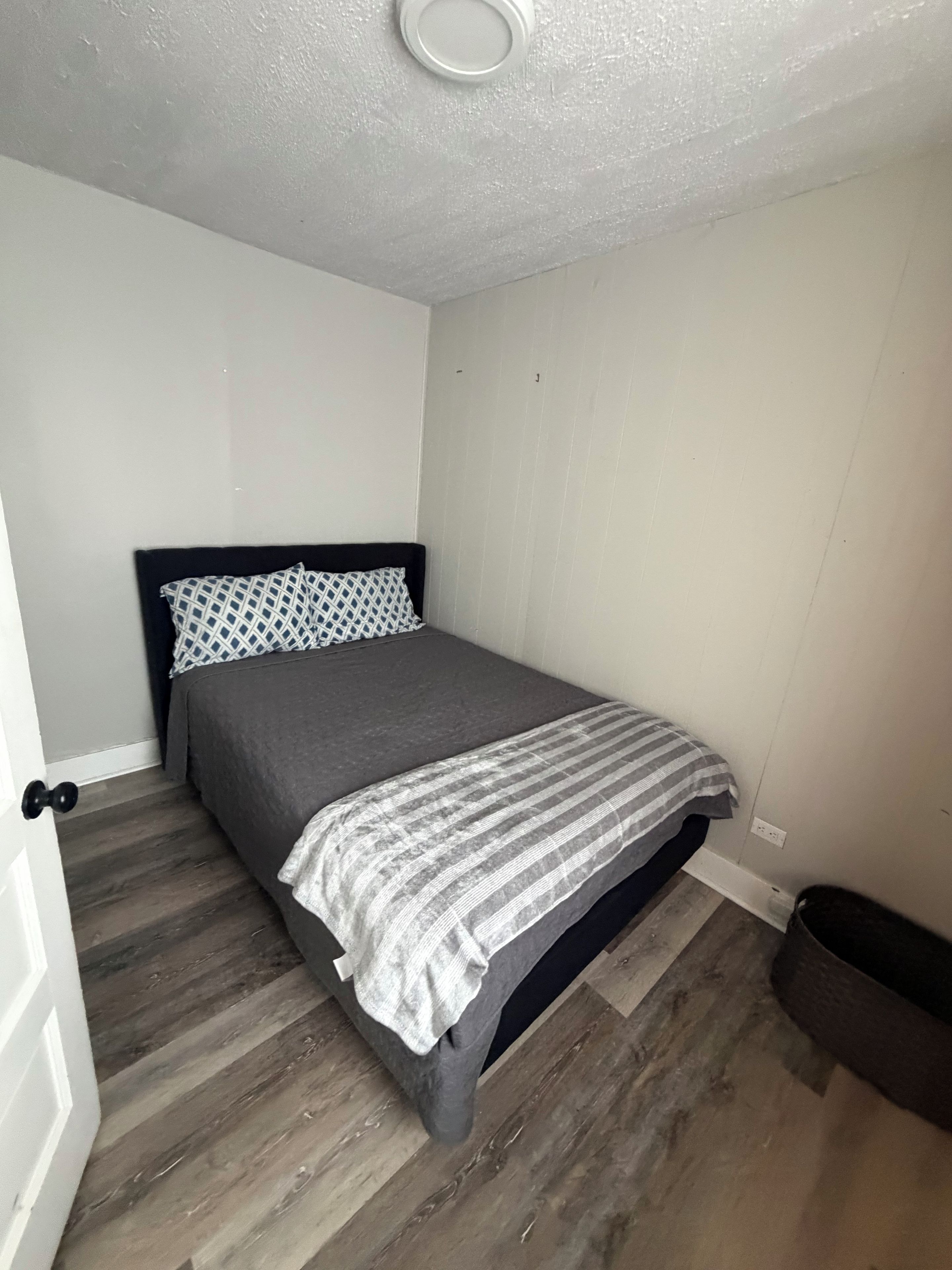 Un dormitorio con una cama, una puerta y un cubo de basura.