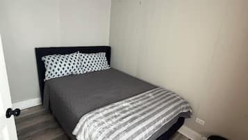 Un dormitorio con una cama, una puerta y un cubo de basura.