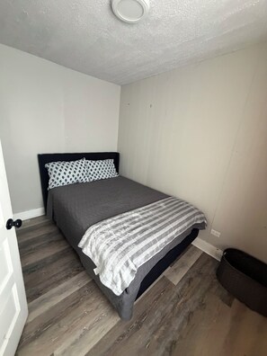 Un dormitorio con una cama, una puerta y un cubo de basura.