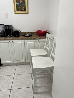 Cocina con armarios blancos, encimera de granito, un tazón rojo y una cafetera.