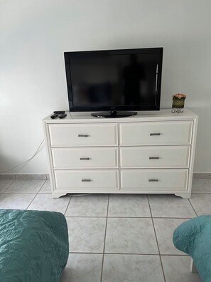 Un mueble blanco para televisor con un televisor de pantalla plana, un control remoto y un adorno en la parte superior.