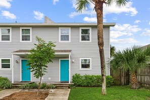 A two-story residential building with a front porch, a blue door, and a small tree in the front yard. - The Yellow Retreat B | Beach Walk + Private Yard (Panama City Beach)