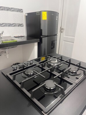 Una cocina con estufa a gas negra, electrodomésticos de acero inoxidable y salpicadero de azulejos blancos.