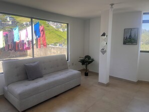 A living room with a sofa, a potted plant, and a view of a hillside with buildings. - New Listing (Quito)