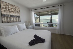 A hotel room with a large bed, a nightstand, a lamp, a view of the sea, and a painting on the wall. - North Shore Haven - Stunning 3 Bdrm Waterfront Home! (Midland)