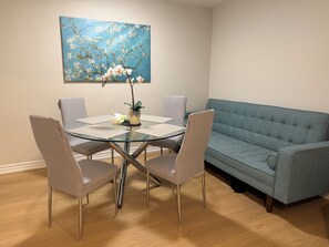 Un coin repas avec une table en verre, quatre chaises, un canapé bleu et un tableau accroché au mur.