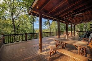 A wooden deck with picnic tables and a hot tub, surrounded by trees and a view of the mountains. - Disconnect at Bearly Connected (Ellijay)