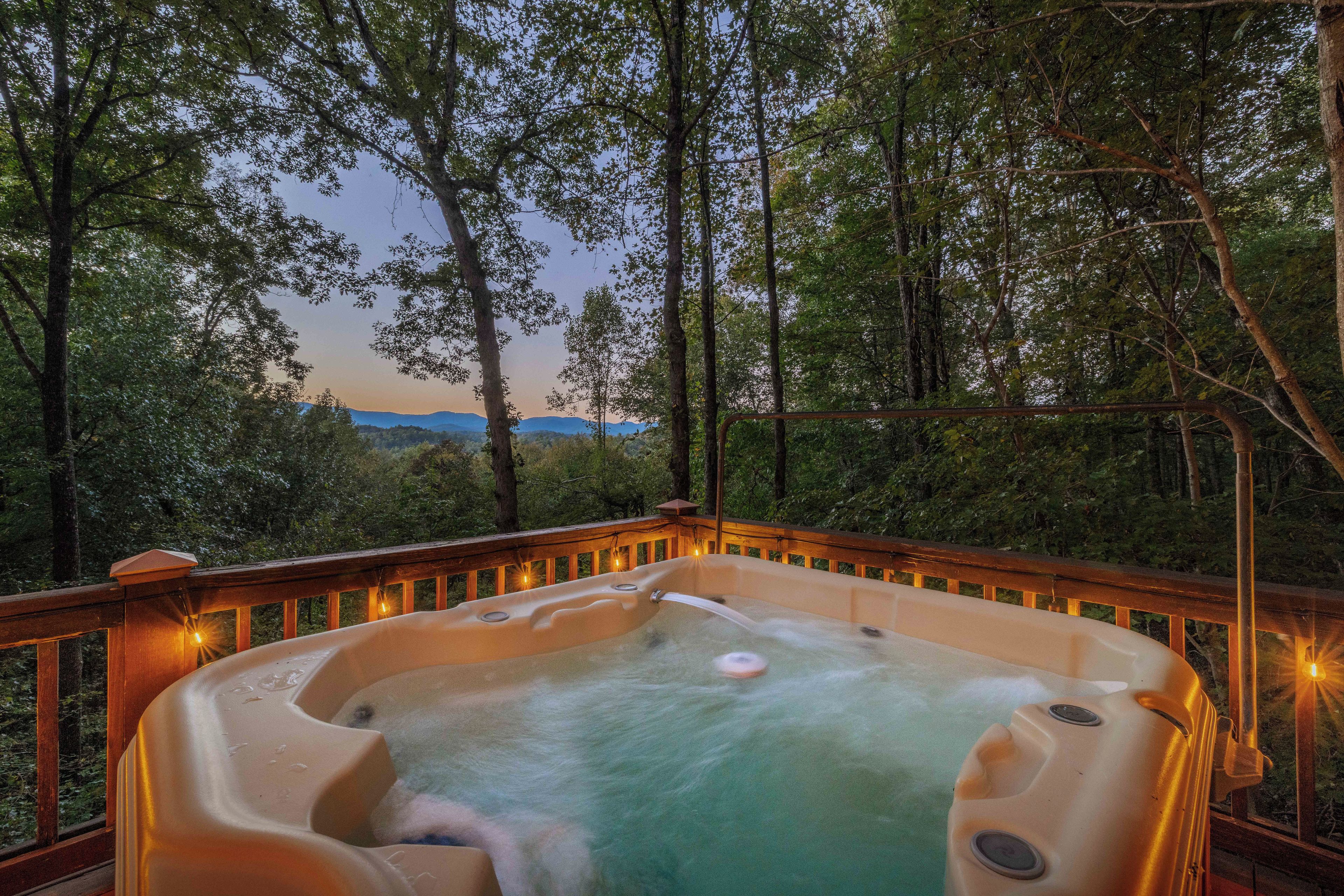 A hot tub on a wooden deck with a view of a forest and mountains in the background.