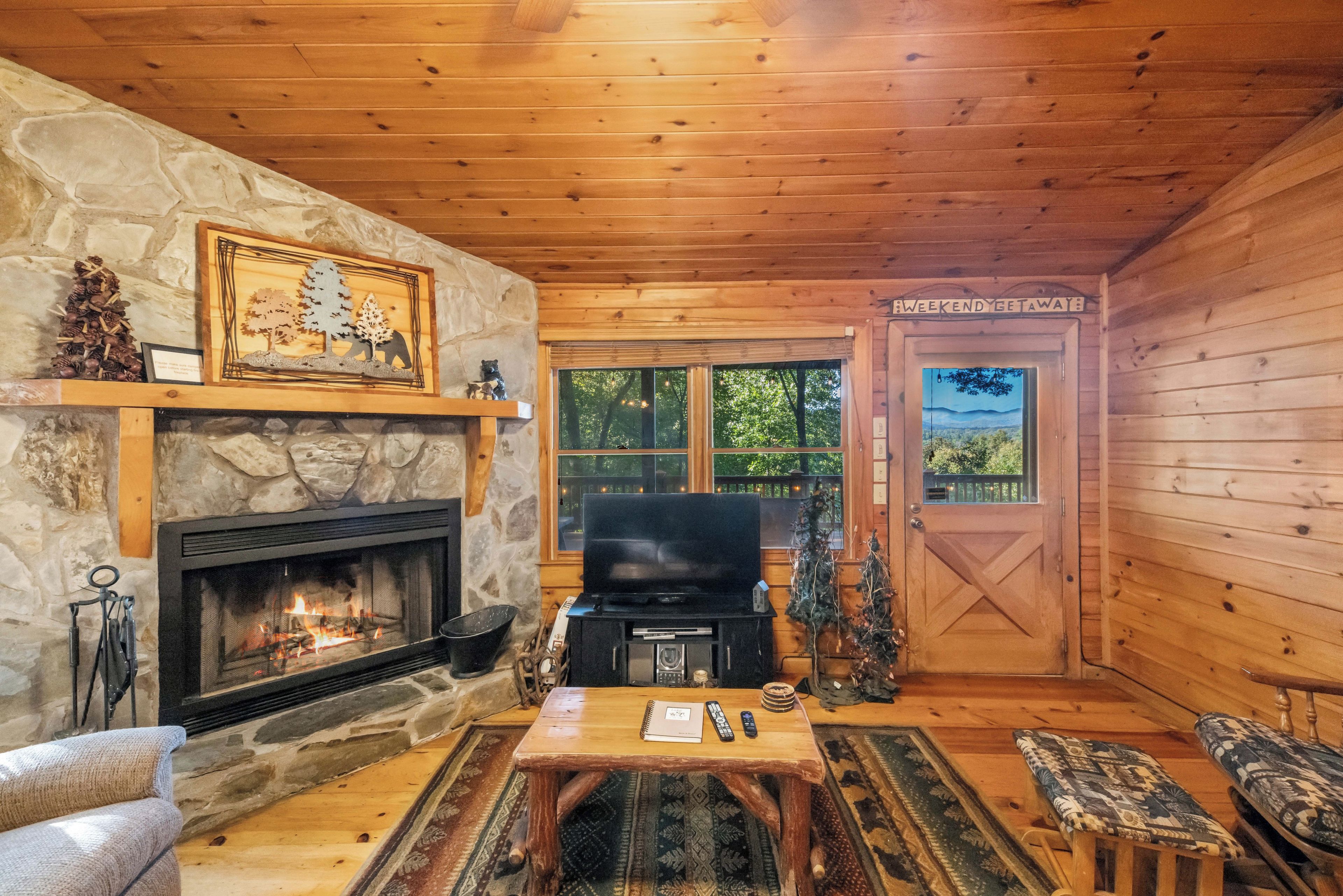 A cozy cabin interior with a stone fireplace, a television, and a wooden door labeled 'Weekend Getaway'.