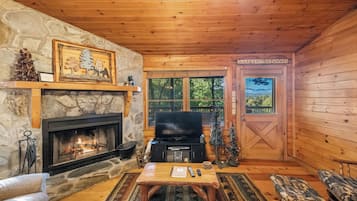 A cozy cabin interior with a stone fireplace, a television, and a wooden door labeled 'Weekend Getaway'.