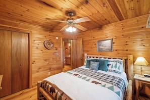 A wooden cabin bedroom with a bed, a ceiling fan, a nightstand, and a lamp. - Disconnect at Bearly Connected (Ellijay)