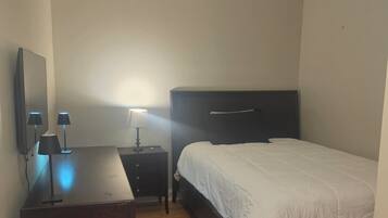 A bedroom with a bed, a desk, a chair, a lamp, and a ceiling light fixture.