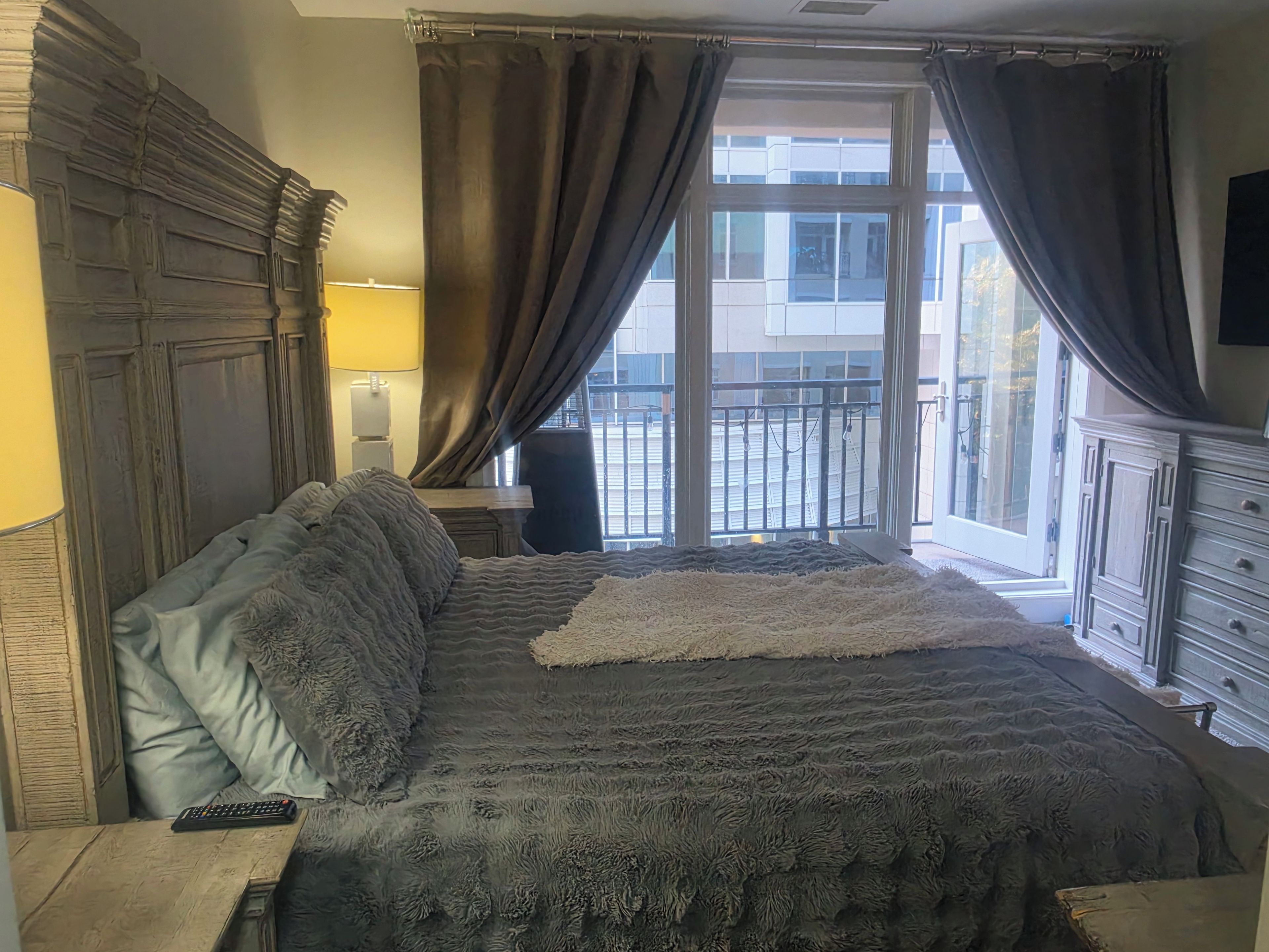 A bedroom with a large bed, a nightstand, a lamp, and a view of the outside through a window.