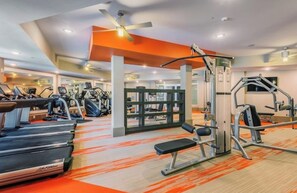 Une salle de sport équipée de tapis de course, d’appareils de musculation et d’un ventilateur de plafond.