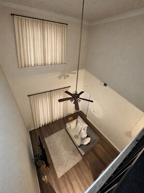 Een moderne woonkamer met een plafondventilator, een bank, een vloerkleed en een raam met gordijnen.