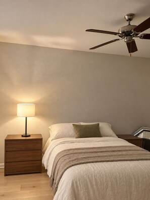 Een slaapkamer met een bed, een nachtkastje met een lamp, een plafondventilator en een houten vloer.