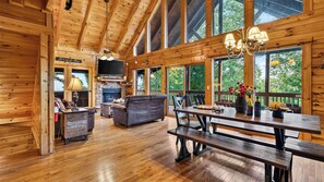 A wooden cabin interior with a fireplace, a sofa, a dining table with benches, and large windows. - Eagles View by Avantstay 5-acre Smoky Cabin Hot Tub + Mountain Views Near Pigeon Forge (Sevierville)
