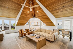 Amplia sala de estar con techo alto, vigas de madera y ventanas grandes que ofrecen vistas del paisaje circundante.
