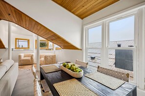 Uma área de refeições com mesa de madeira, jogos americanos trançados e um arranjo de plantas verdes.