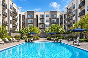 A swimming pool with lounge chairs and umbrellas, surrounded by multi-story buildings with balconies. - Stylish 2BR King Suite Near Uptown (Charlotte)