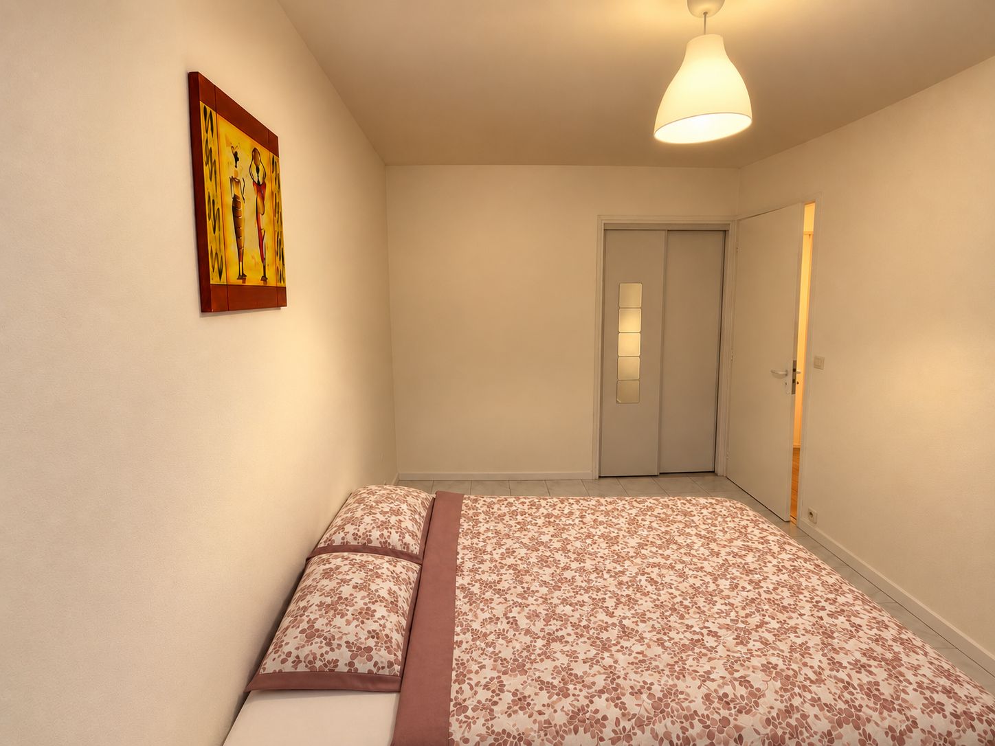 Une chambre à coucher avec un lit, une porte et un luminaire fixé au mur.
