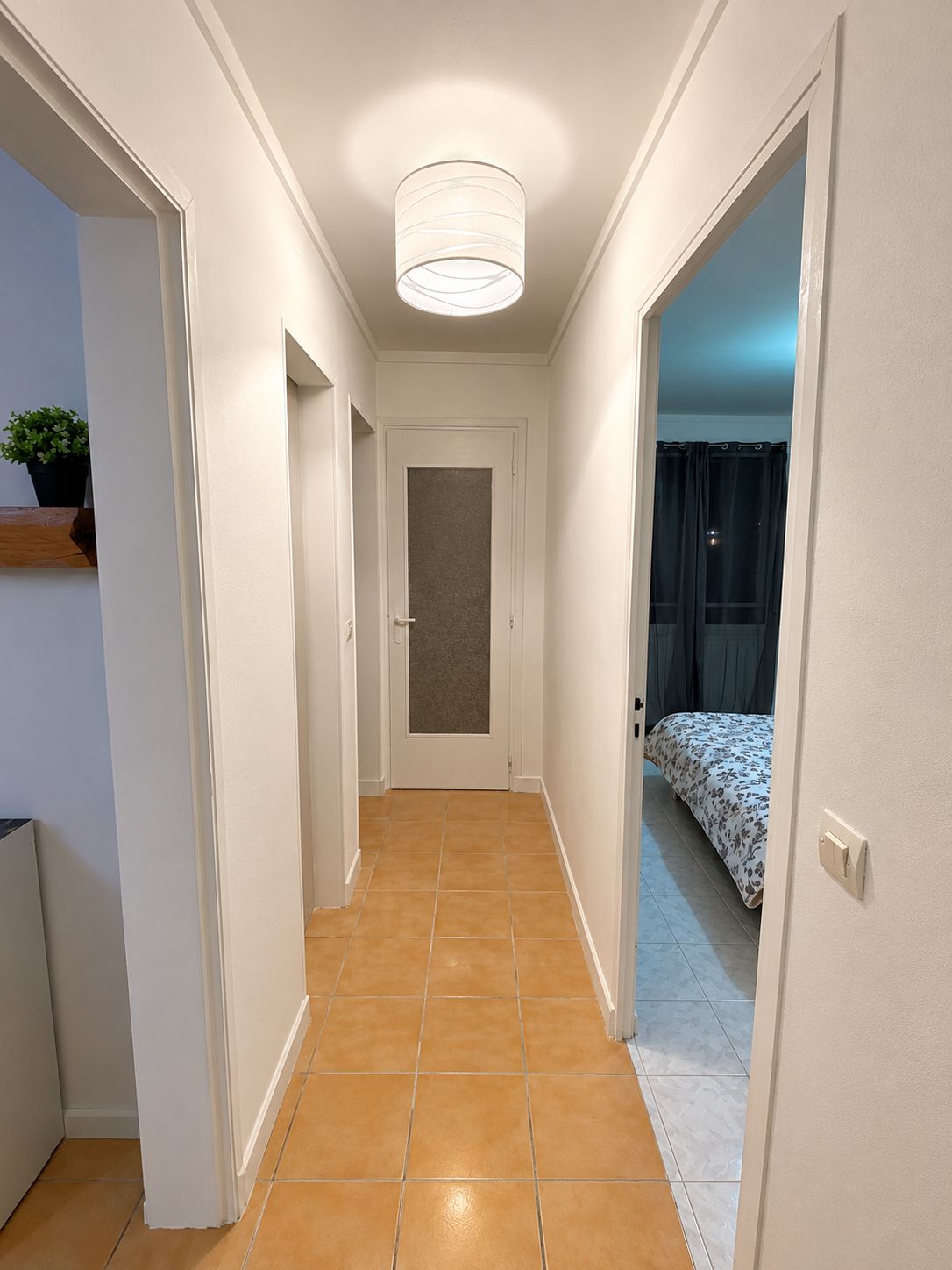 Ein schmaler Flur mit einer Tür am Ende, der zu einem Zimmer mit einem Bett führt.