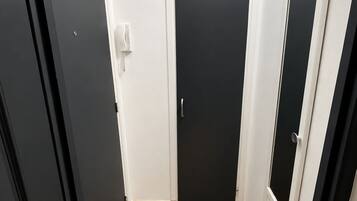 En hall med ett klinkergolv, en svart dörr och en vit vägg med en ljusströmbrytare.
