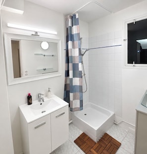 Ein modernes Badezimmer mit einem weißen Waschtisch, einer Dusche mit blauer und weißer Karomuster-Duschvorhang, einem raumhohen Fenster und einer weißen Badewanne.