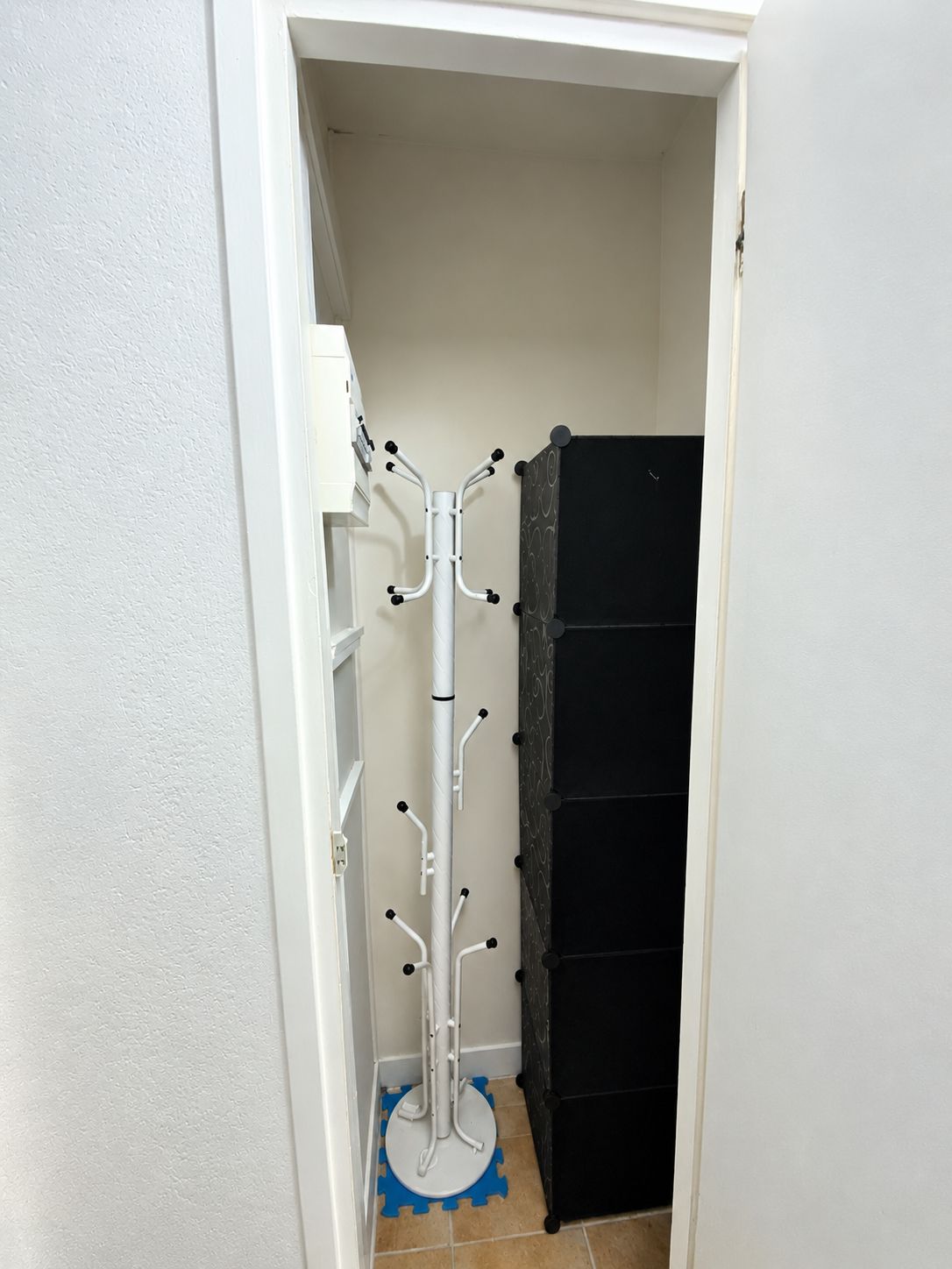 En smal hall med en vit dörr, en svart förvaringsenhet och en vit klädhängare med flera krokar.