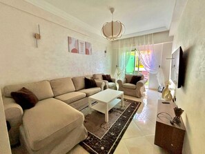 A living room with a sofa, coffee table, and a TV mounted on the wall. - Beau cocon meublé, 2Bd sécurisé  Wi-Fi  Près Rabat (Témara)