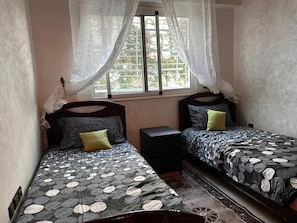 A bedroom with two beds, a nightstand, and a window with sheer curtains. - Beau cocon meublé, 2Bd sécurisé  Wi-Fi  Près Rabat (Témara)